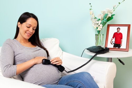 A pregnant woman holding a telephone to her belly.