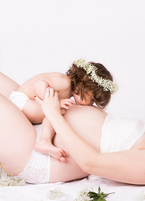 embarazada-tumbada-con-hija-besando-la-barriga