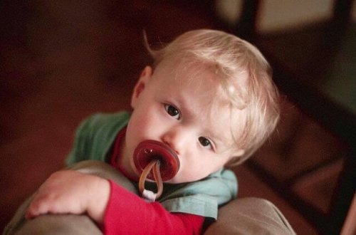 A baby using a pacifier and looking up at his parent.