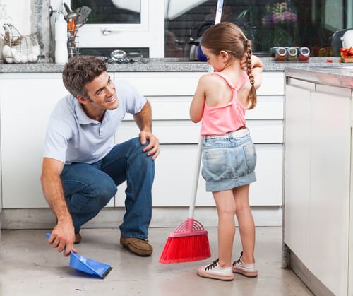 A little girl helping her dad sweep the kitchen.