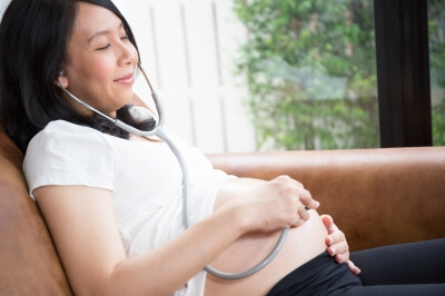 Une femme enceinte qui écoute les battements du coeur du bébé dans le ventre avec un stéthoscope. 