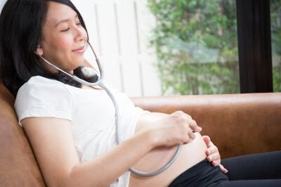 Une femme enceinte qui écoute les battements du coeur du bébé dans le ventre avec un stéthoscope.