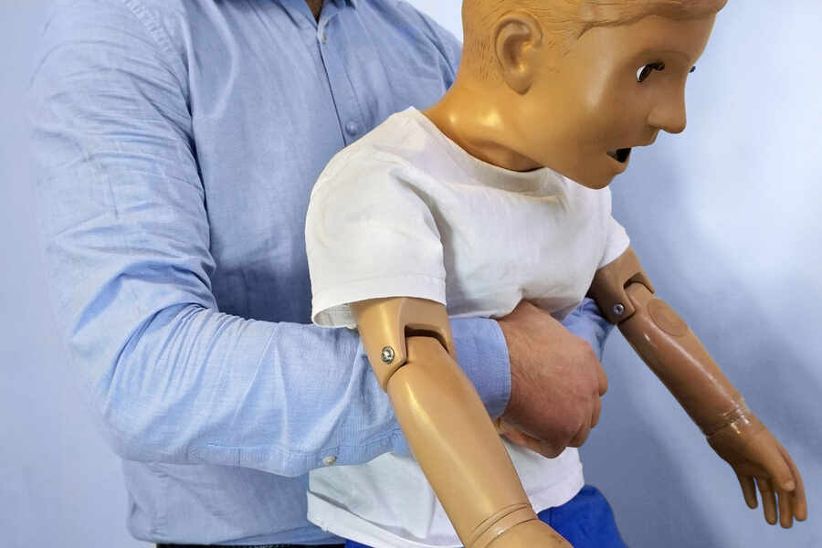 A man practicing the heimlich maneuver on a dummy.