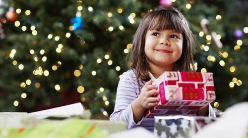 Niña con un regalo bajo el árbol de navidad