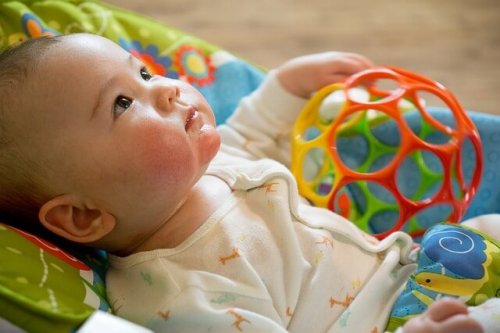 A baby looking up while touching a toy.