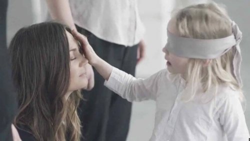 Et barn med bind for øynene berører morens ansikt.