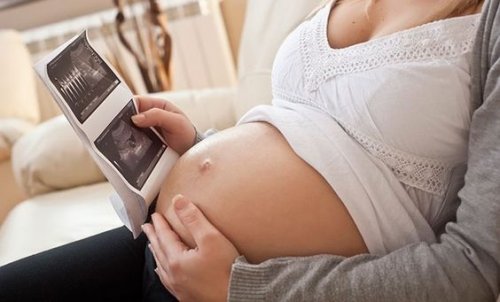 A mother touching her pregnant belly and looking at an ultrasound image.