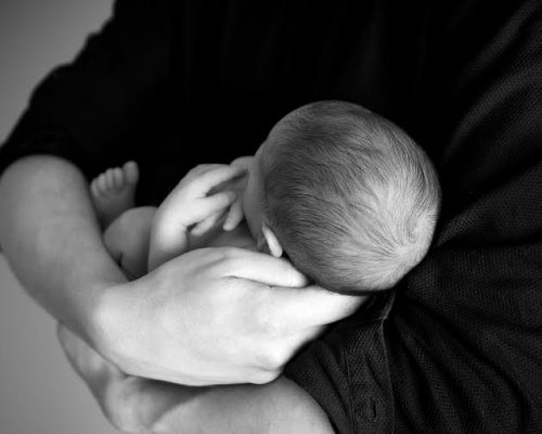 A newborn sleeping in his parent's arms.