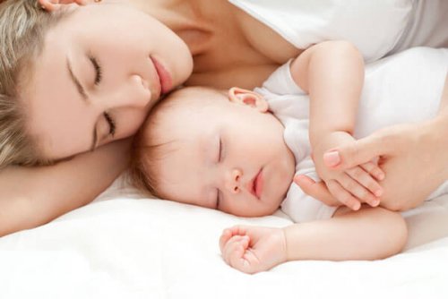 Äiti nukkuu käsivarsi kiedottuna nukkuvan vauvansa ympärille.