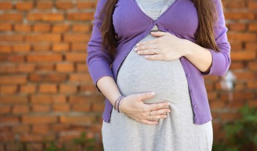 Outdoor portrait of beautiful pregnant woman holding her belly, brick wall in background