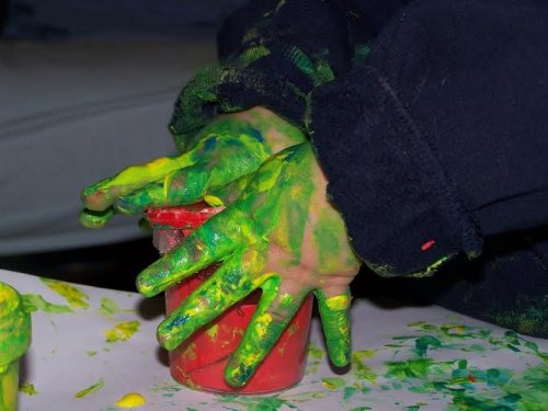 A toddler with their hands covered in green and yellow paint.