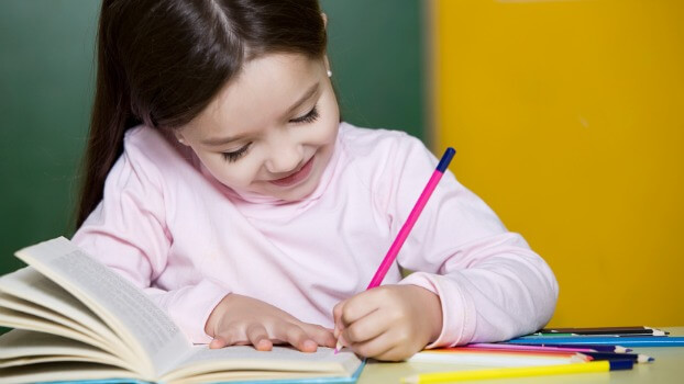 Petite fille heureuse de travailler, avec un crayon et un livre 