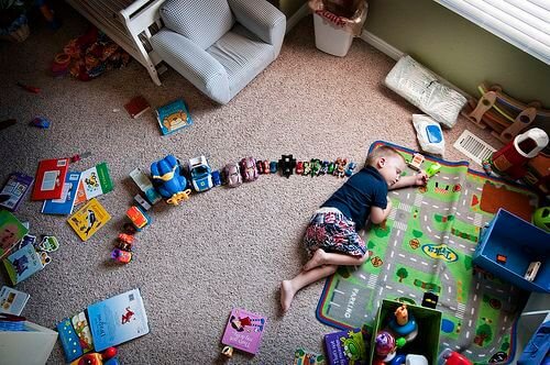 Un enfant allongé au milieu de ses jouets dans sa chambre.
