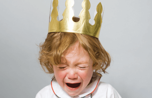 A little boy wearing a paper crown and crying.