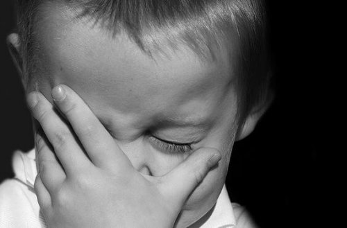 A toddler covering his face and looking upset.