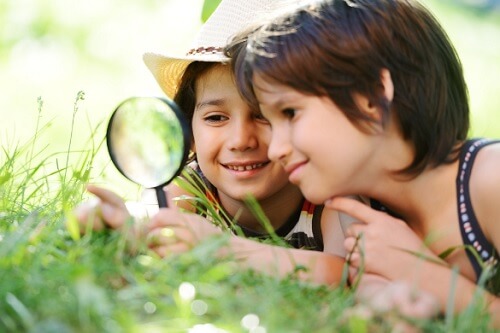 Two young boys looking at grass with a magnifying glass.