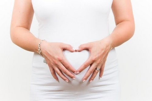 A woman making the shape of a heart with her hand over her pregnant belly.