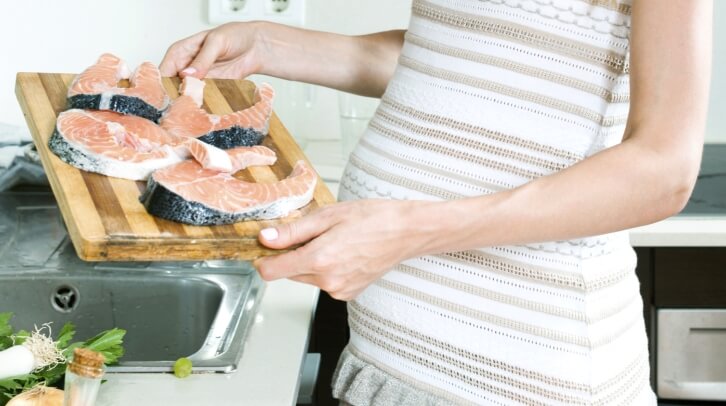 A pregnant woman preparing salmon.