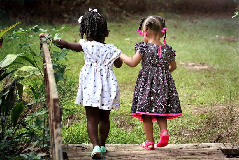 Two little girls holdinghands and crossing a wooden bridge together.