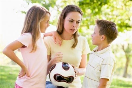 En kvinne som holder en fotball som forklarer reglene for to barn.