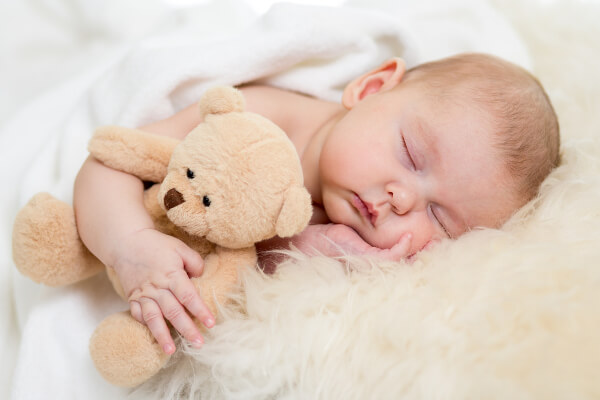 Bébé endormi dans son berceau étreignant un ours en peluche.