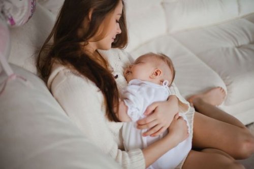 Une mère assise dans un canapé avec son bébé qui dort dans ses bras.