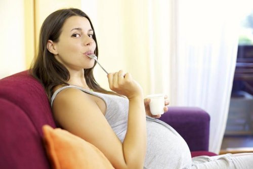 Happy pregnant woman at home eating white yogurt