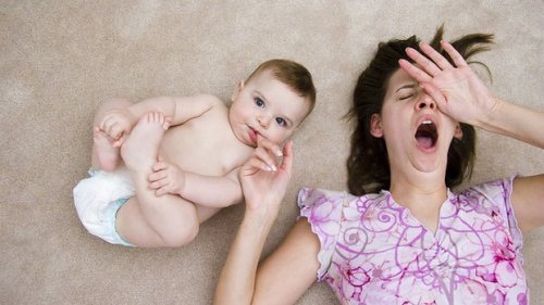 A mother yawning while her baby sucks on her finger.