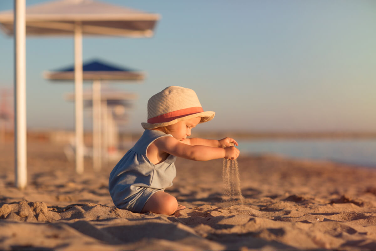 Niño con gorro jugando con la arena de la playa