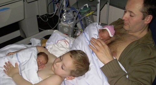 En far og hans unge sønn gir hud-mot-hud-kontakt til nyfødte tvillinger.
