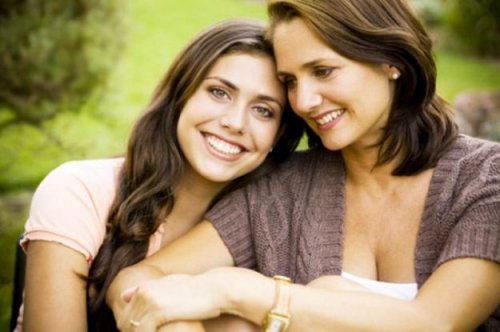 A teenage firl leaning on her mother's shoulder and smiling.