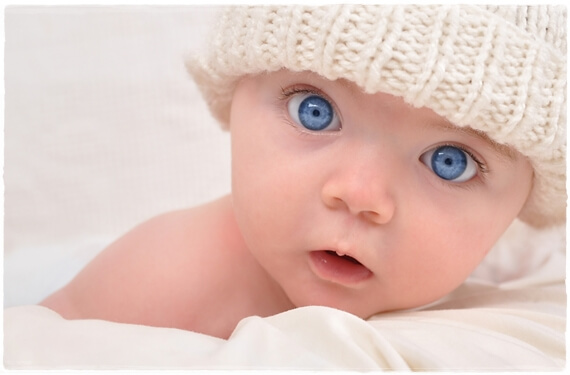 En bebis med stora blå ögon bär en stickad mössa.