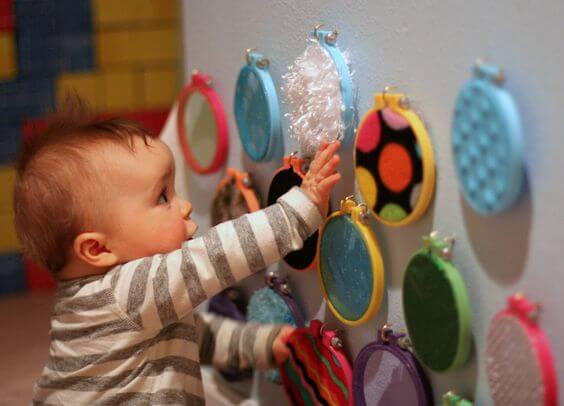 Un bébé qui touche des matières différentes sur un mur d'éveil. 