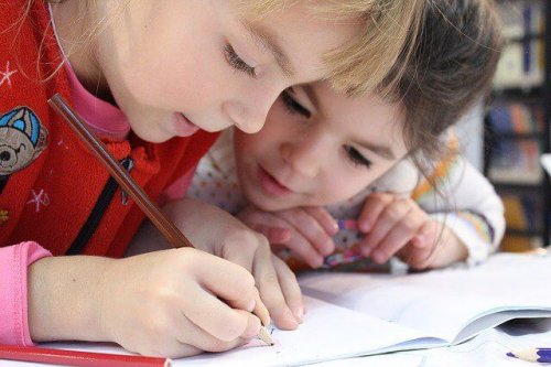 Two young girls at school writing in a notebook.
