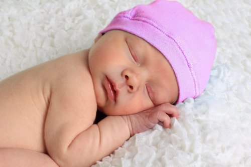 A newborn sleeping with a pink cap on.