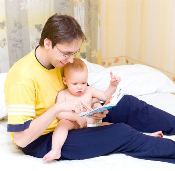 Un père avec son bébé dans les bras qui regardent un livre. 