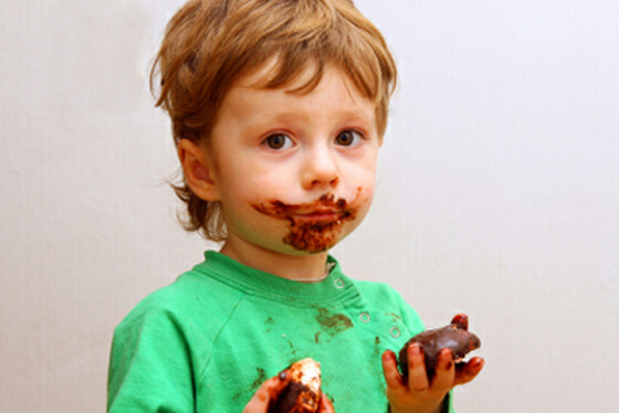 A while eating chocolate, with chocolate all over his face, hands, and shirt.