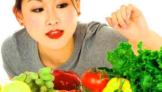 Une femme mange des fruits et légumes.