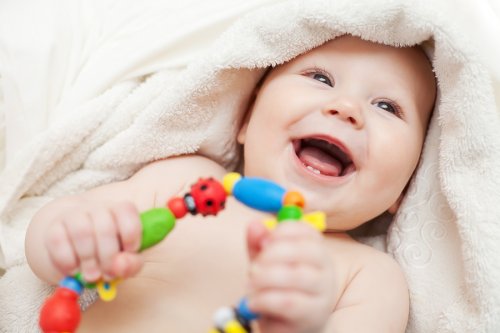Bebé sonriendo envuelto en una toalla tras un baño sujeta un sonajero. 