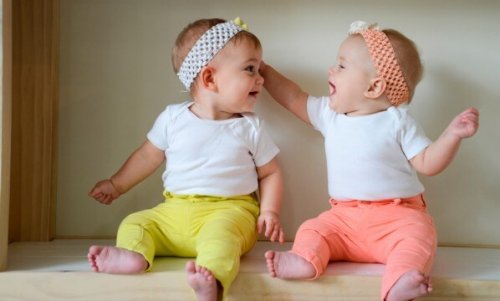 Twin baby girls wearing coordinating outfits and smiling at eachother.