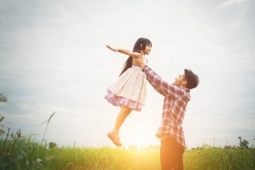 Padre elevando a su hija en el aire en el campo y poniendo en práctica la disciplina positiva.