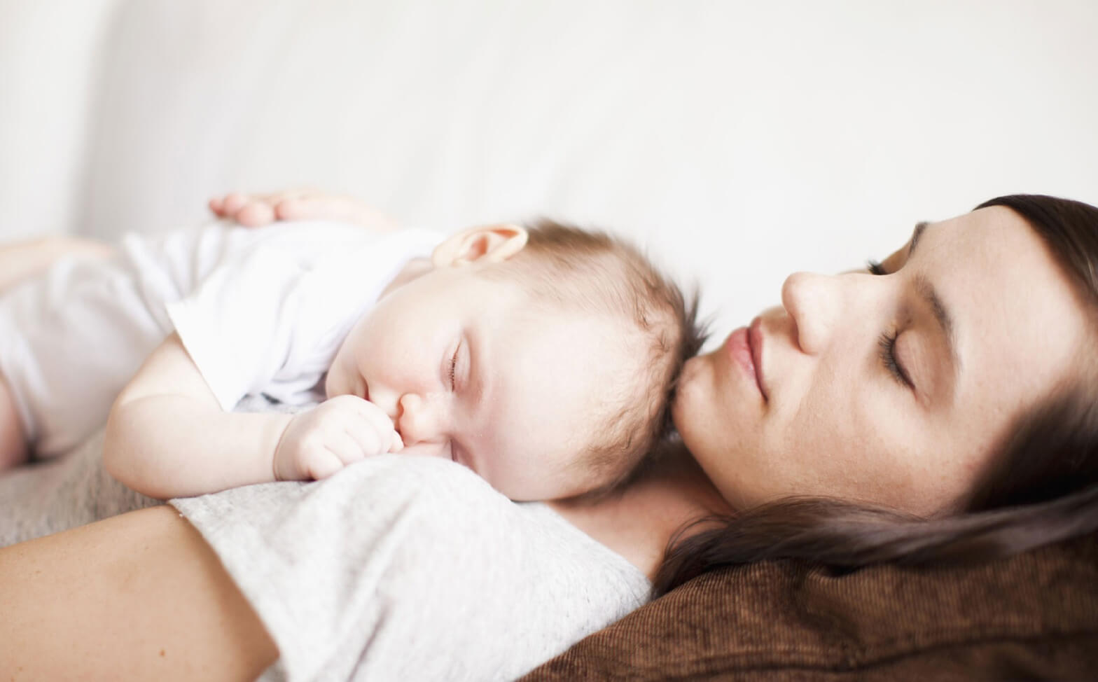 A woman napping with her baby on her chest.