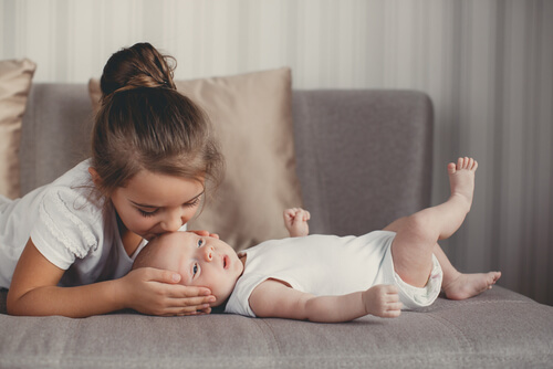 A big sister kissing her baby sibling on the forehead.