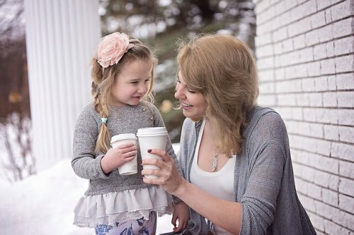 A mother and her daughter drinking from paper coffee cups in the snow.