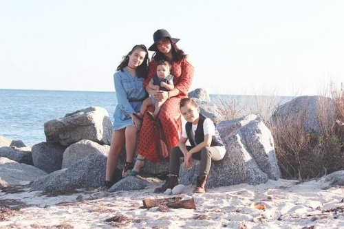 En mamma och hennes tre barn poserar för en bild på stranden.