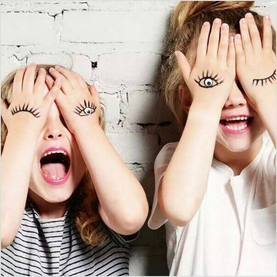 Deux enfants qui sourient en se cachant les yeux.