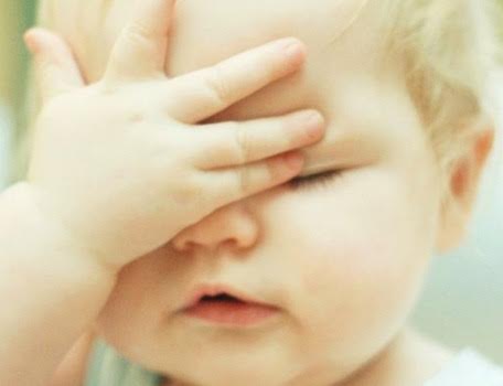 Un bébé qui met sa main sur son visage.