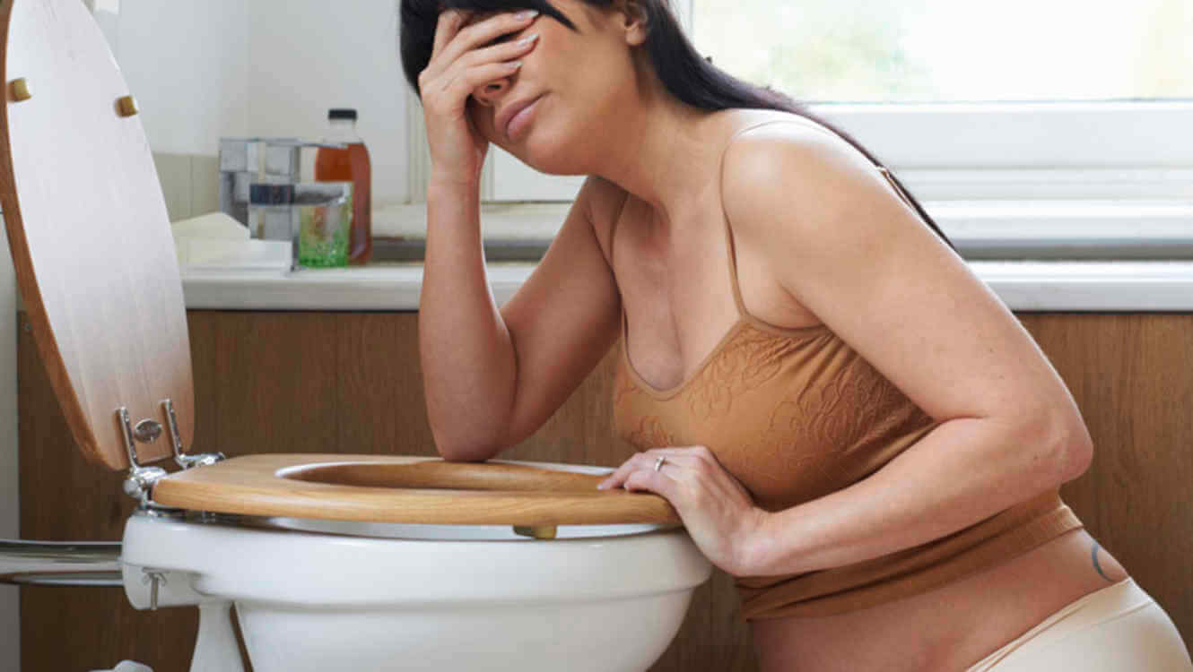 Femme enceinte dans sa salle de bain, prise de nausées au-dessus des toilettes