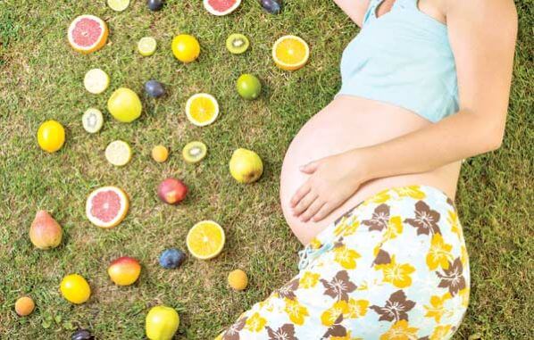 Une femme enceinte allongée avec des fruits à ses côtés. 