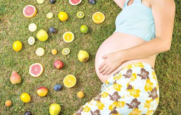 Une femme enceinte allongée avec des fruits à ses côtés.